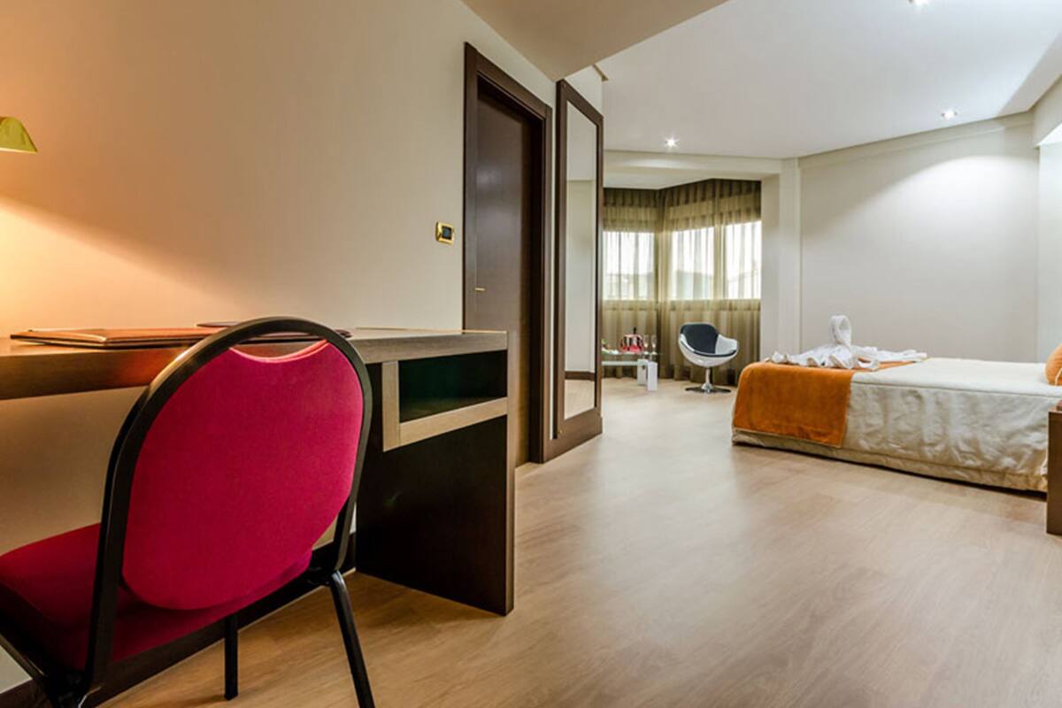A hotel room with a desk, chair, bed, and a window with curtains.