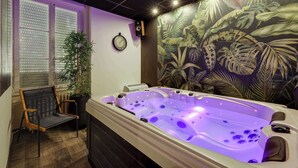 Une salle de spa équipée d’un jacuzzi, d’une horloge et d’une fresque murale aux motifs tropicaux.