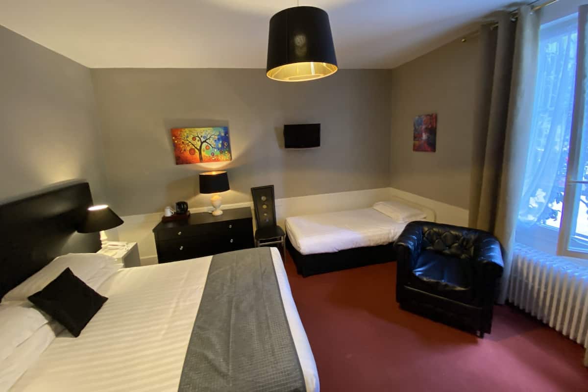 Une chambre d’hôtel avec un grand lit, un lit plus petit, un fauteuil en cuir noir, un bureau avec une lampe et des œuvres d’art accrochées aux murs.