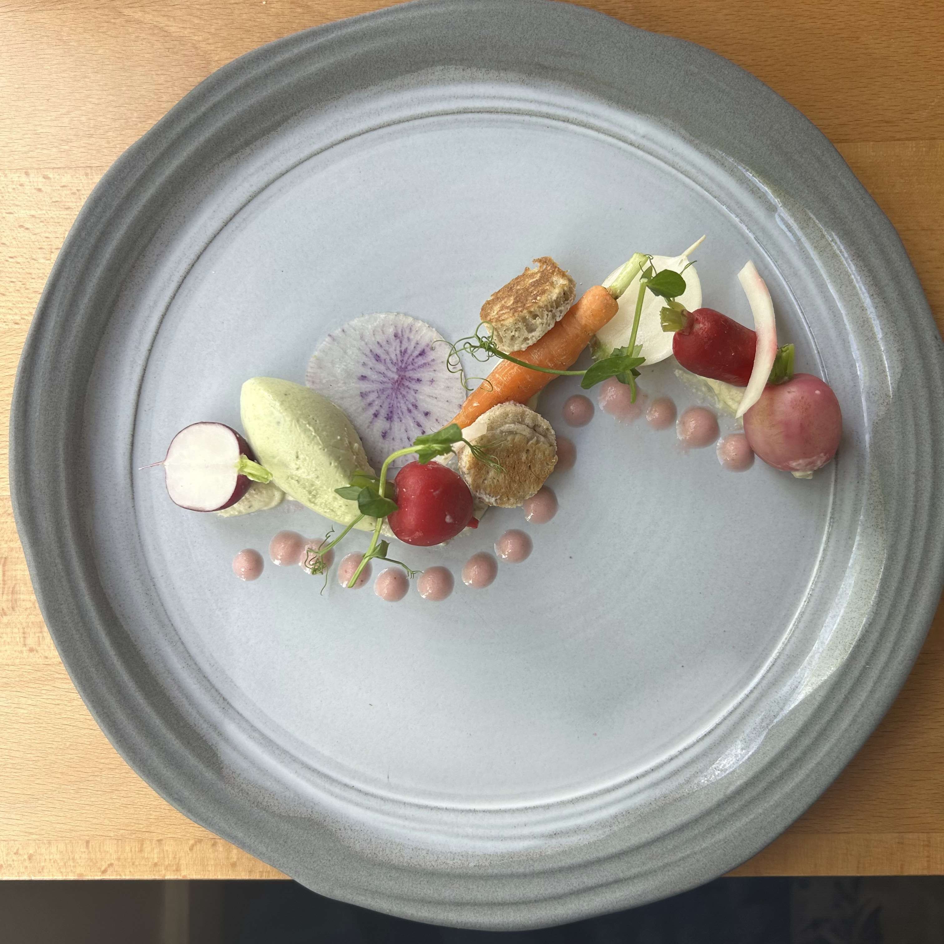 Une assiette contenant divers aliments, notamment des radis, des raisins et une tranche de radis ornée de motifs violets.