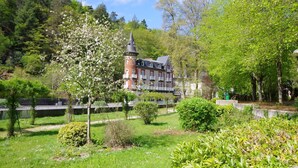 Un bâtiment historique doté d’une tour, entouré d’une végétation luxuriante et d’un petit étang.