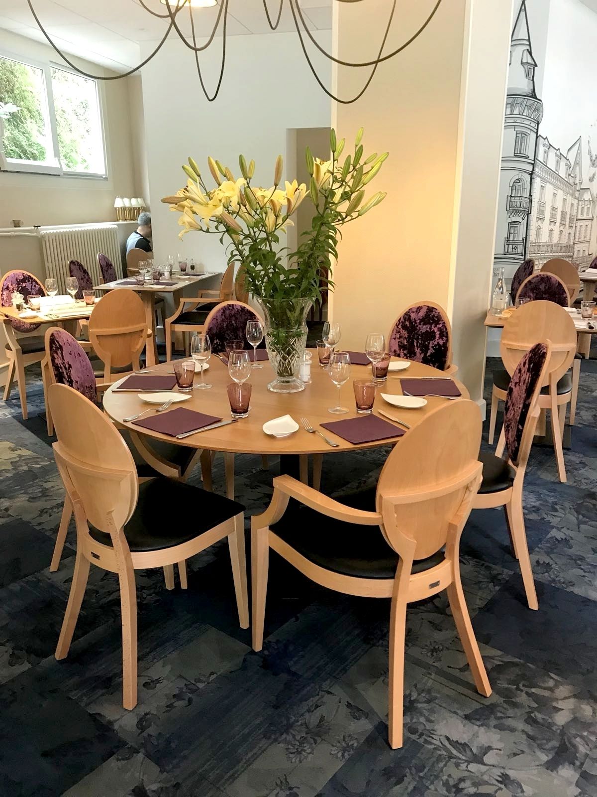 Ein Essbereich mit runden Tischen, Holzstühlen und einer Vase mit gelben Blumen.