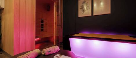 Un cuarto de spa con una puerta de madera, una recepción con iluminación morada y dos láminas botánicas enmarcadas en la pared.