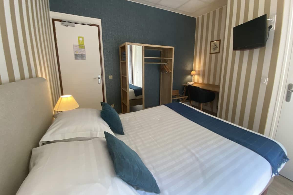 Une chambre d’hôtel comprenant un lit, un bureau, un miroir, une télévision et une armoire.