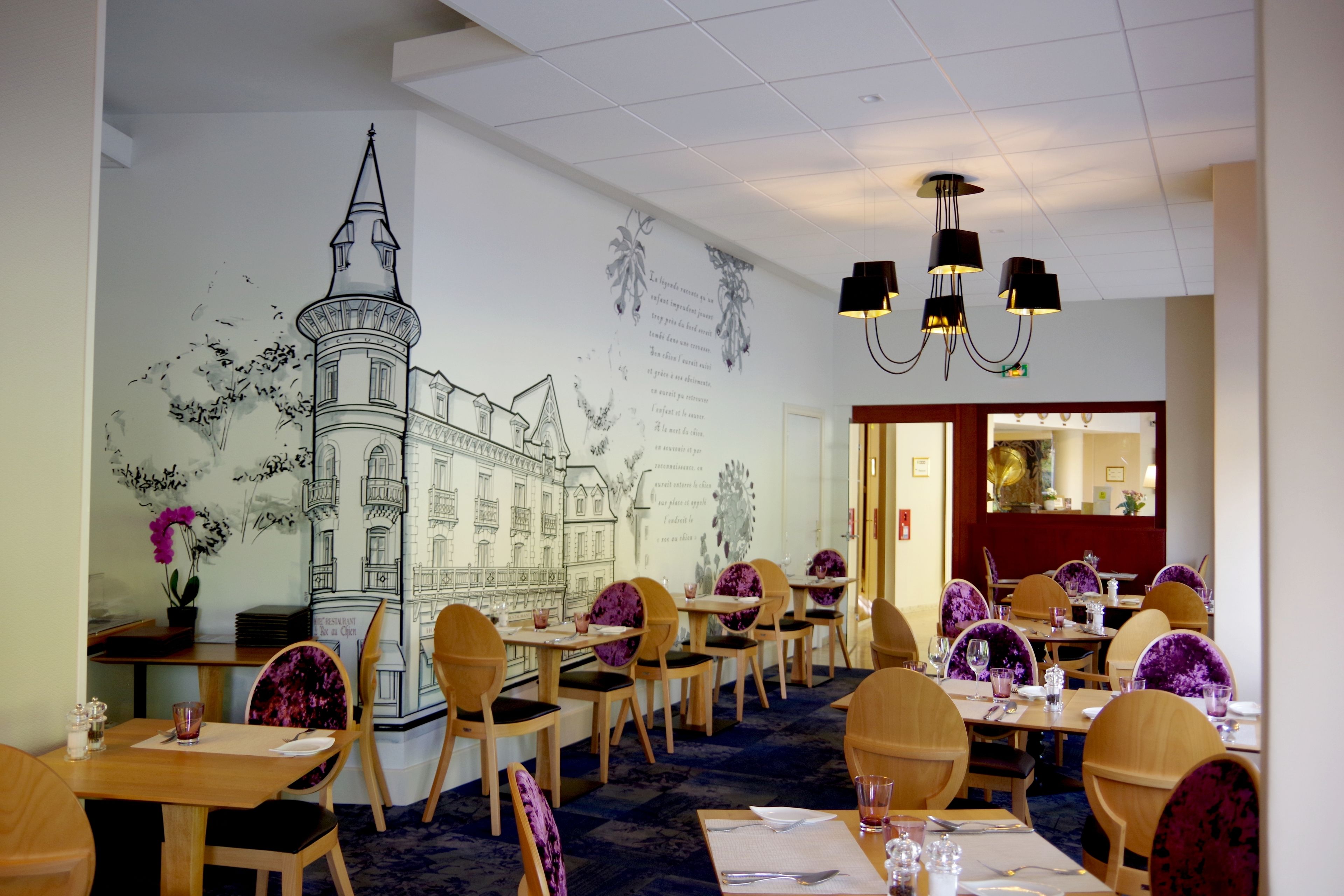 A restaurant with wooden tables and chairs, a mural of a building, and black pendant lights.