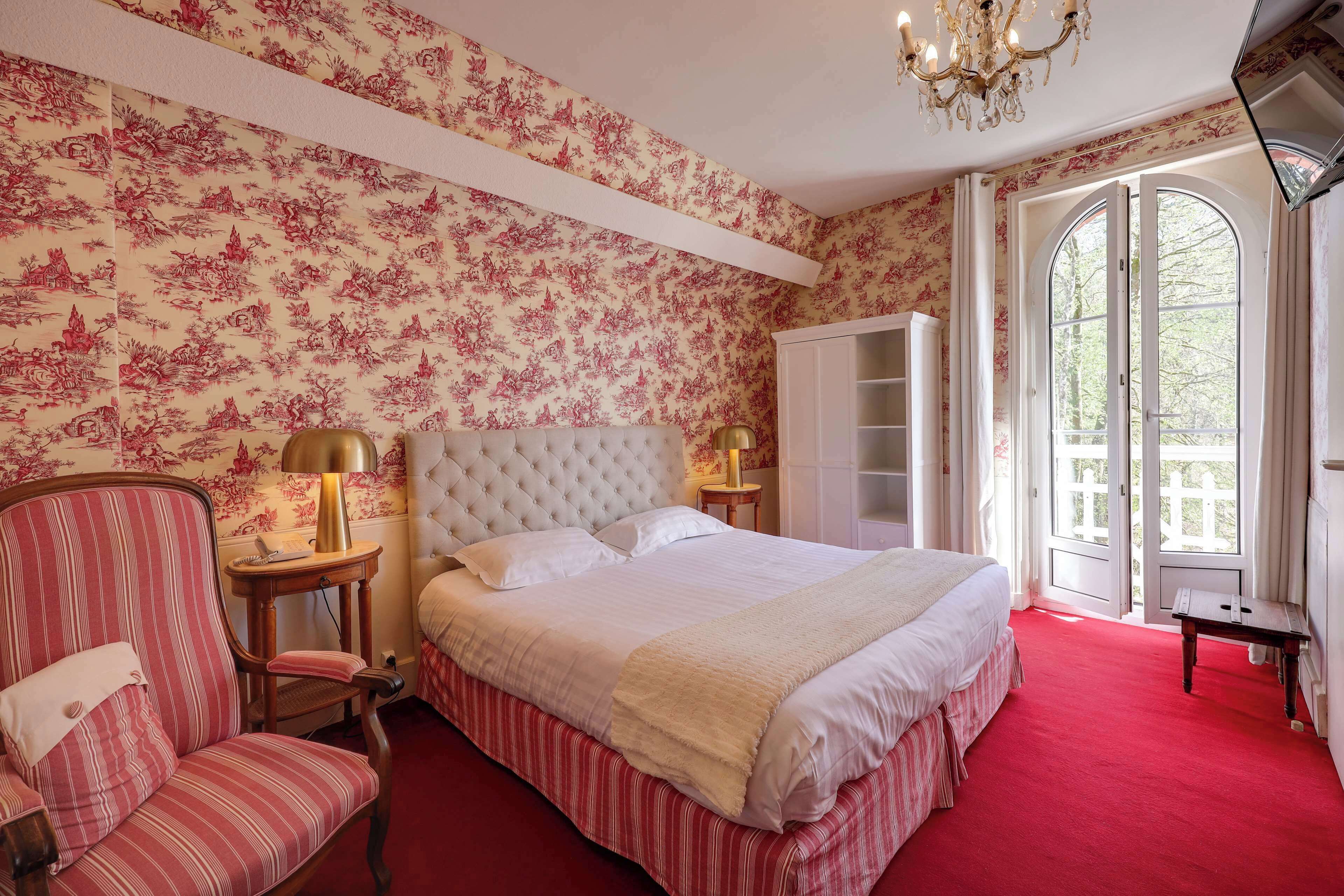 A bedroom with a large bed, a chair, a nightstand, a wardrobe, and a view of the outdoors through a door.