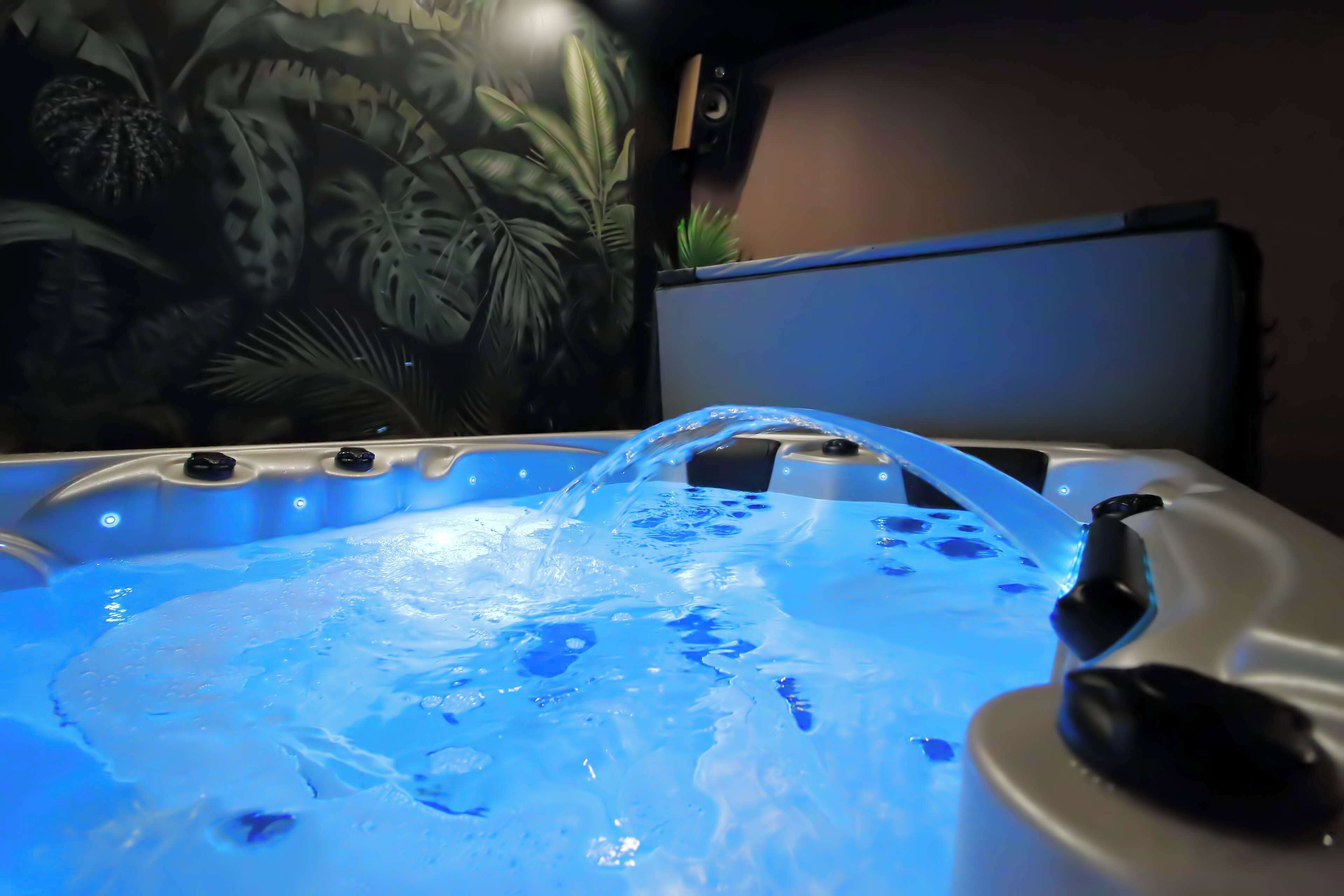Un jacuzzi con caída de agua, rodeado por un mural tropical.