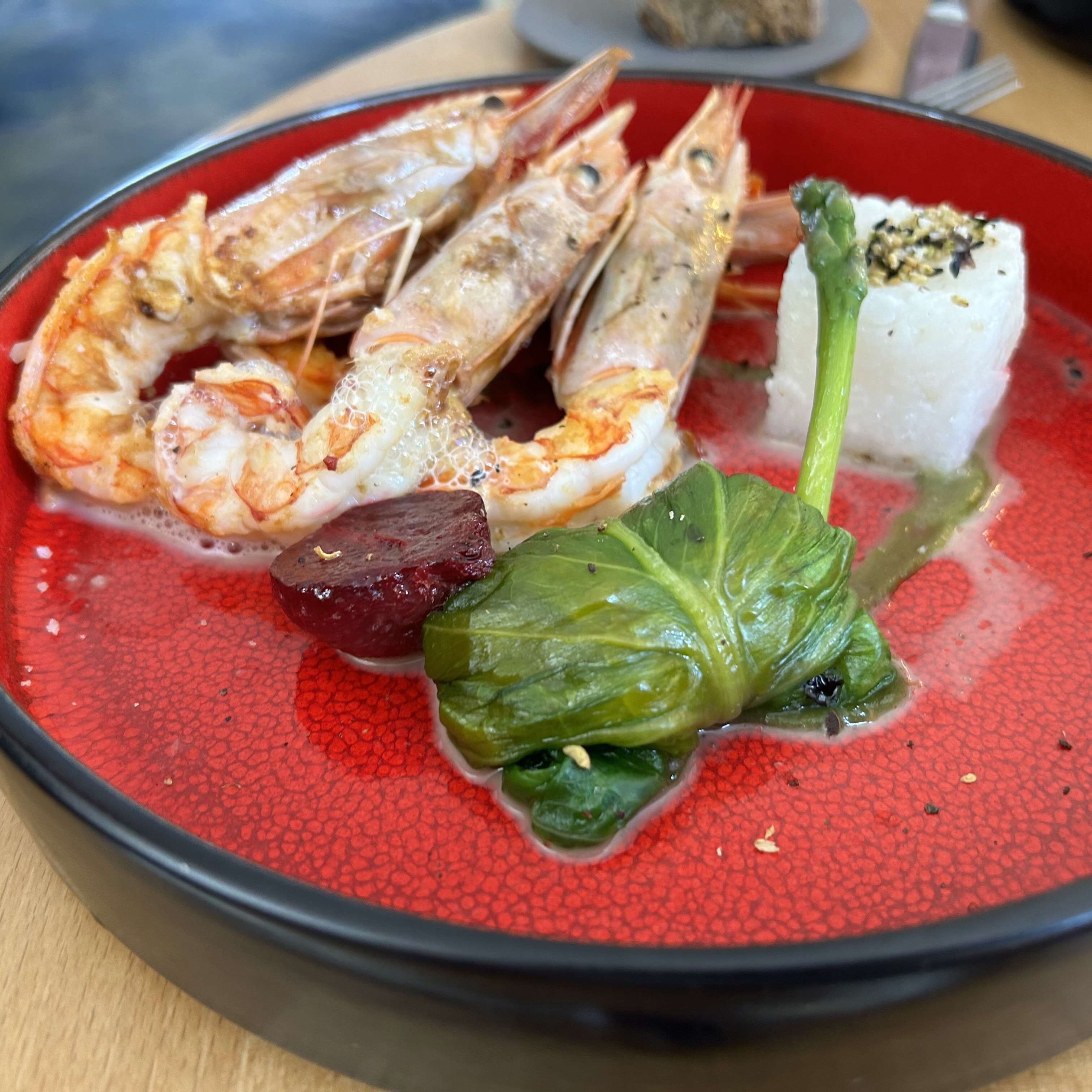 Un plato con camarones, un trozo de carne y hojas verdes.