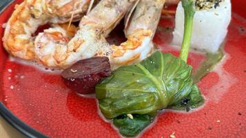 Un plato con camarones, un trozo de carne y hojas verdes.