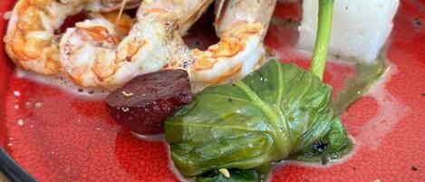 Un plato con camarones, un trozo de carne y hojas verdes.