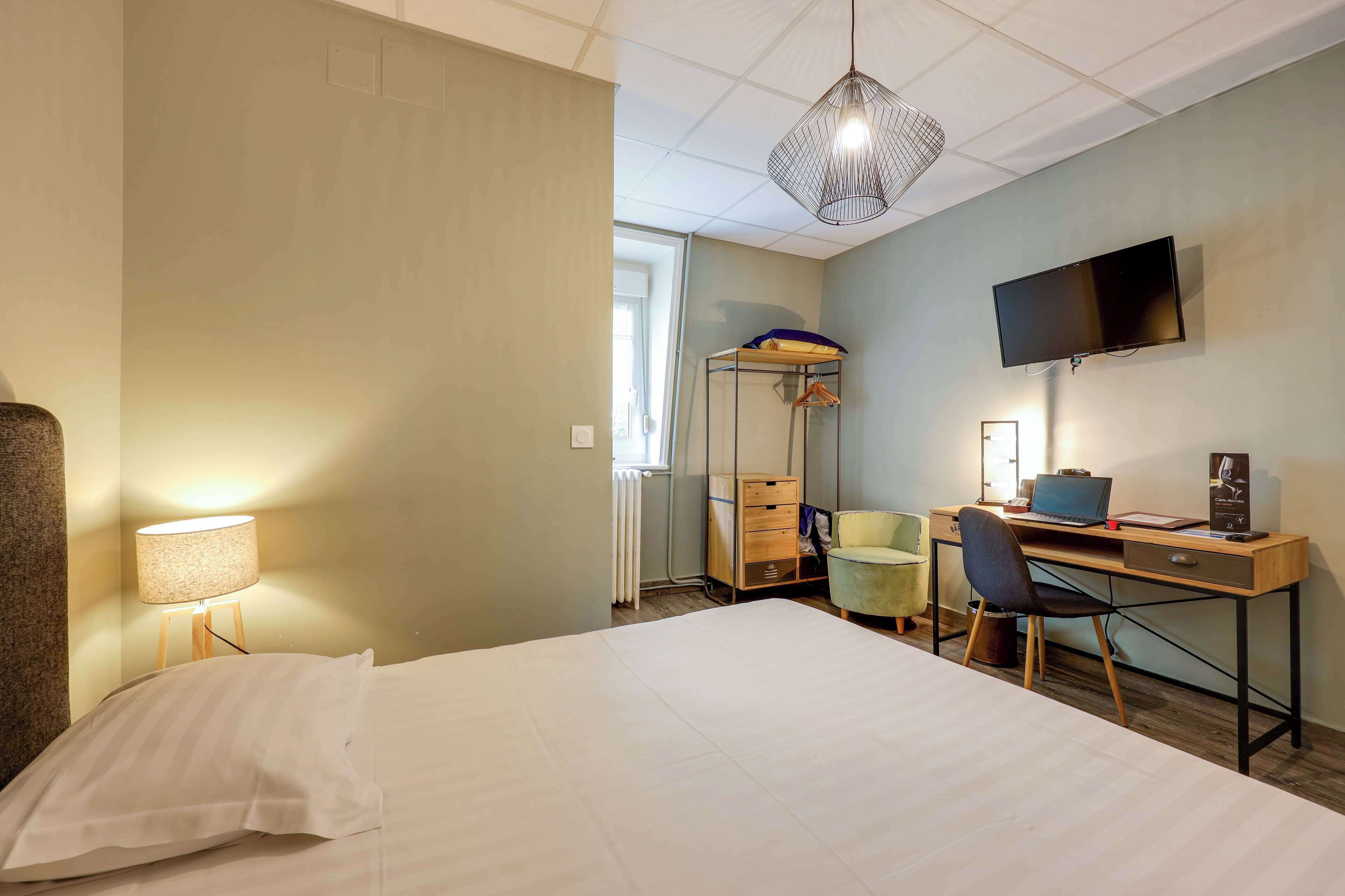 Quarto de hotel com cama, escrivaninha, cadeira, televisão, abajur e radiador.