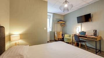 Quarto de hotel com cama, escrivaninha, cadeira, televisão, abajur e radiador.