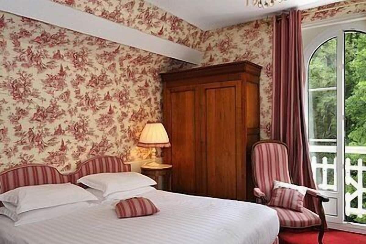Une chambre à coucher comprenant un lit, une chaise, une table de chevet et une fenêtre donnant sur un paysage verdoyant.