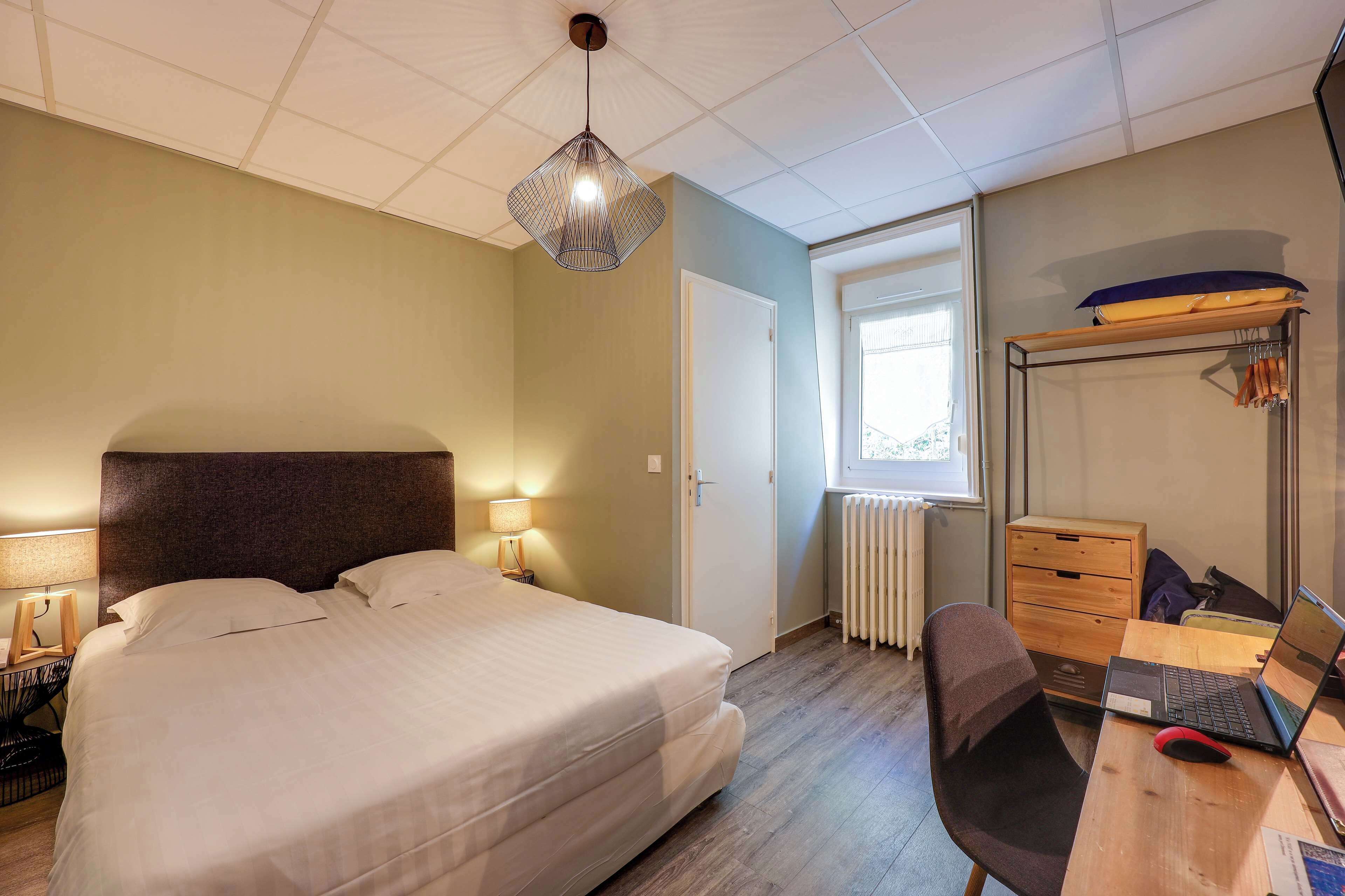 A bedroom with a bed, bedside lamps, a desk with a laptop, and a wardrobe.