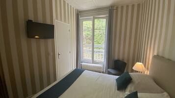Hotelkamer met gestreepte behang, een bed met wit en donkerblauwe beddengoed, een aan de muur bevestigde televisie, een raam met uitzicht op groen en een stoel bij het raam.