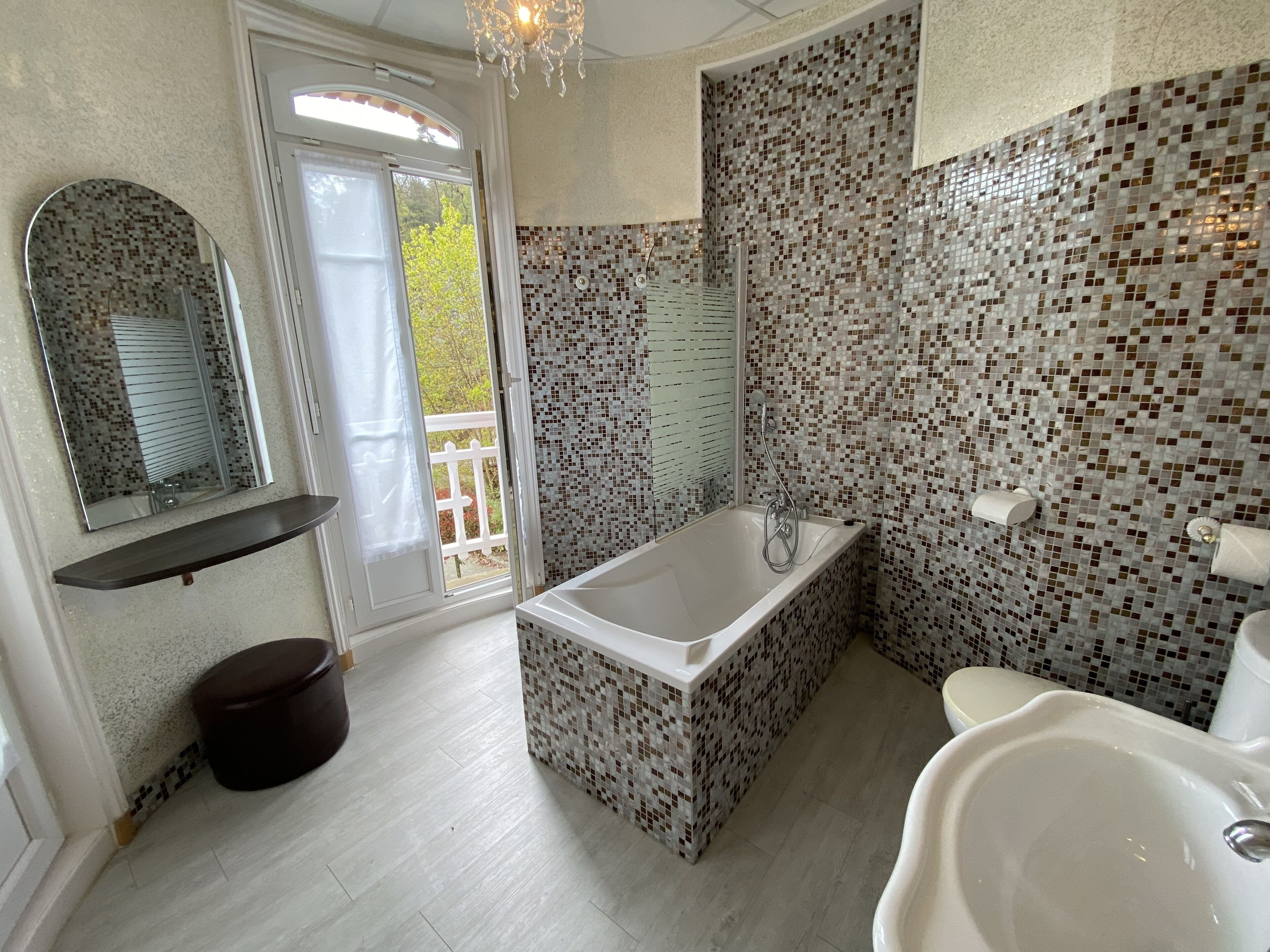 A modern bathroom with a freestanding bathtub, a large mirror, and mosaic tile walls.