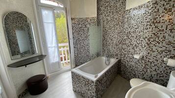A modern bathroom with a freestanding bathtub, a large mirror, and mosaic tile walls.