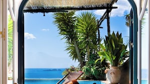 A view from a room with a large window overlooking a pool area with lounge chairs and tropical plants. - VILLA FIORENTINO POSITANO  (Positano)