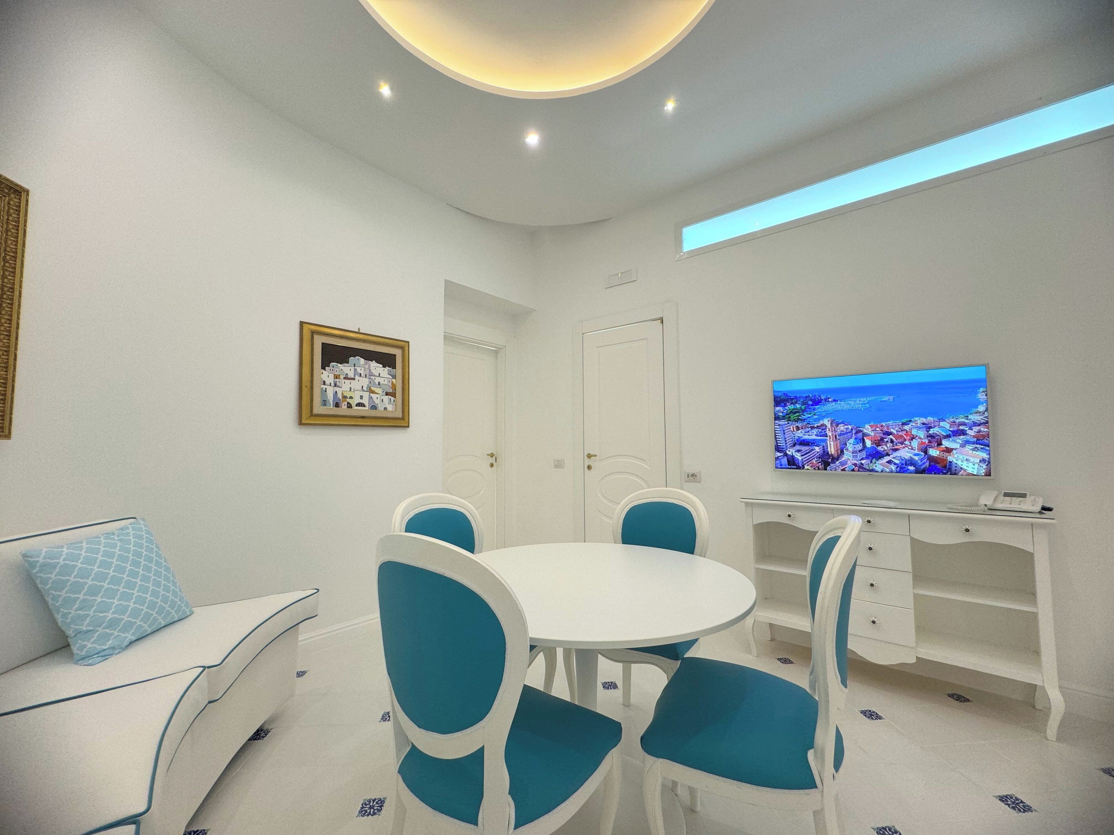 A modern room with a round dining table, four chairs, a sofa, a TV, and a door.