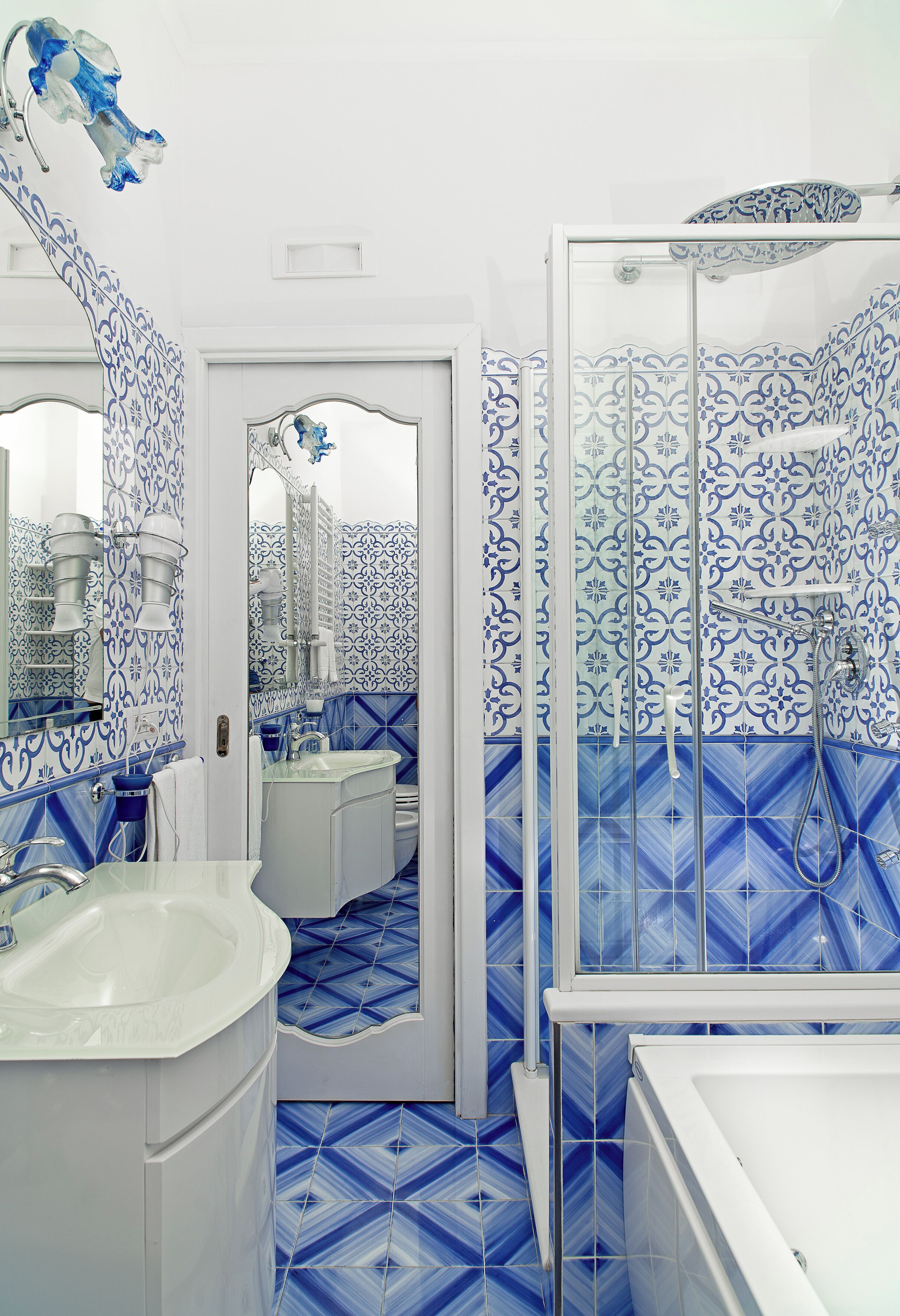 A bathroom with a white sink, a mirror, and a shower area with blue patterned tiles.