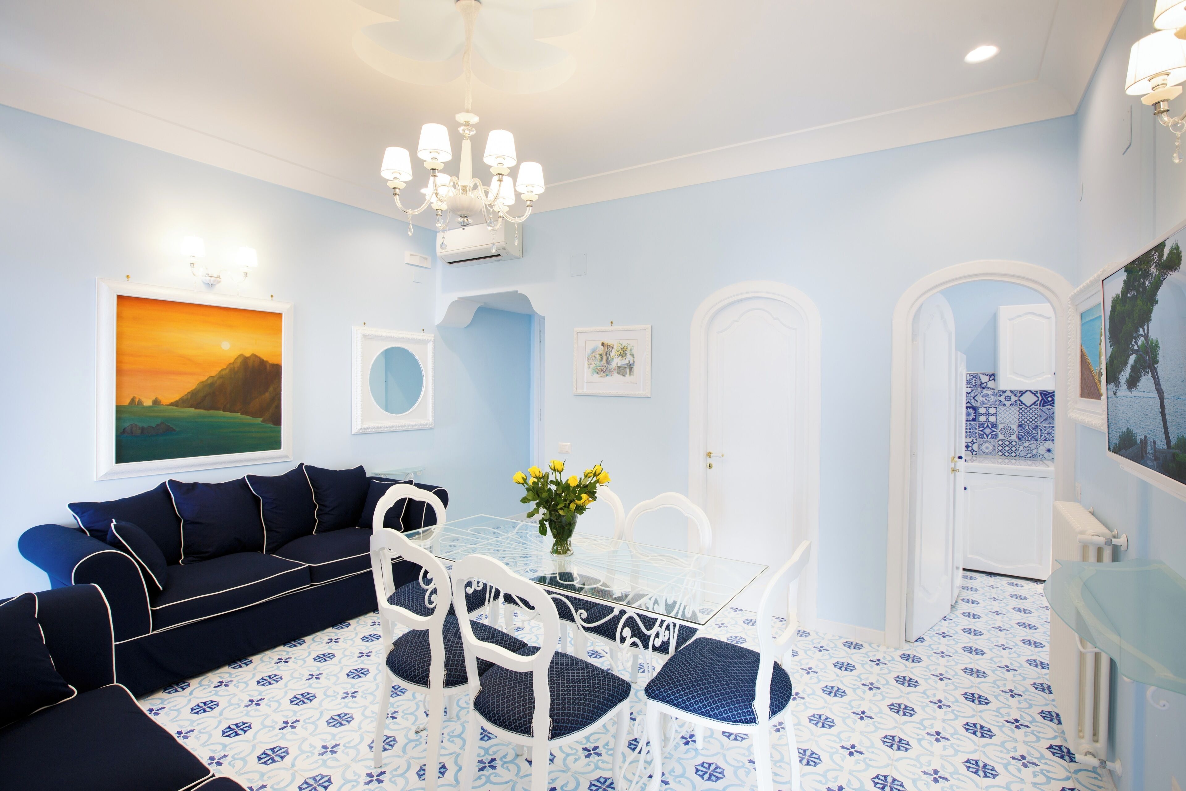 Ein Zimmer mit blauer und weißer Farbgestaltung, ausgestattet mit einer Couch, einem Esstisch, Stühlen und einer Chandelüster.