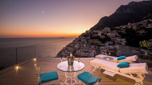 A terrace with a table, two lounge chairs, and a view of a coastal town at sunset. - VILLA FIORENTINO POSITANO  (Positano)