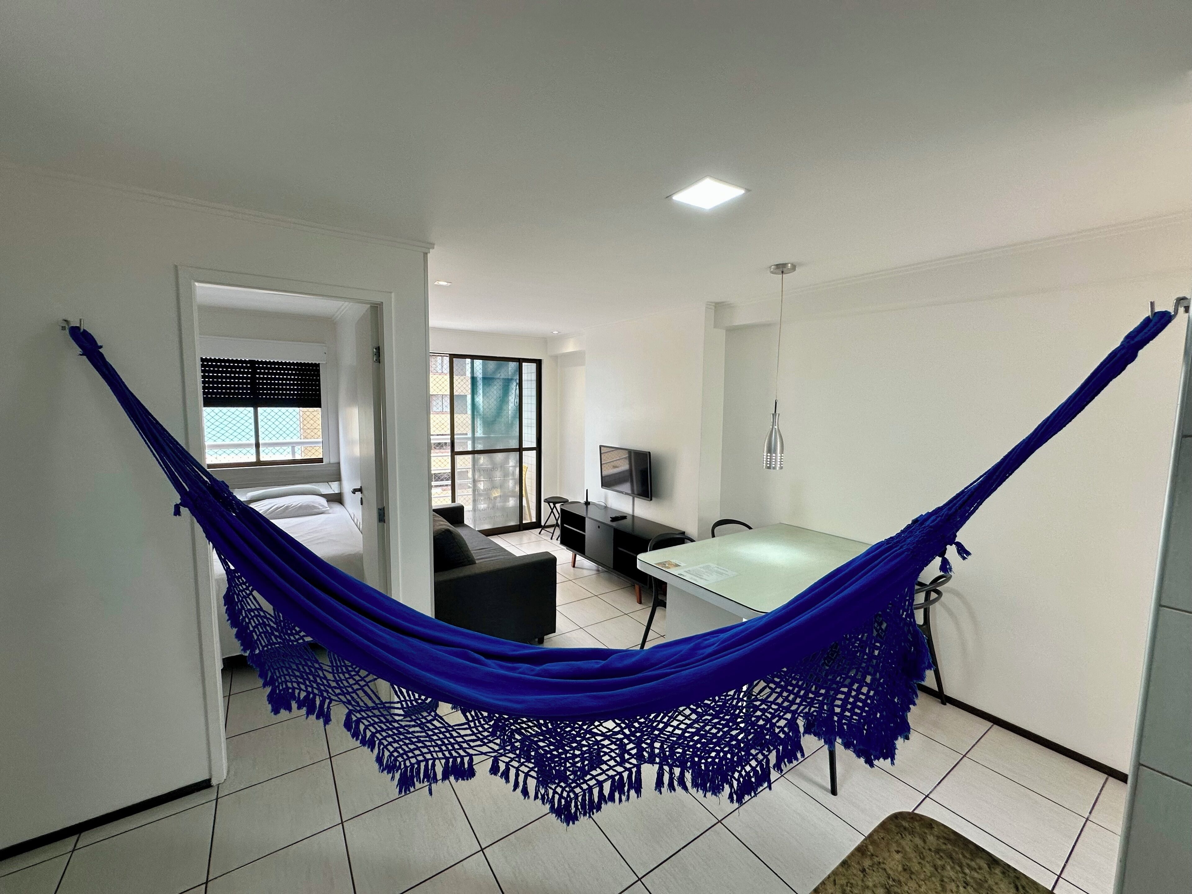 Een kamer met een hangmat, een bed, een bureau en een televisie.