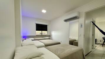 Habitación de hotel con tres camas, una ventana con persianas, un equipo de aire acondicionado y una escalera que conduce a otra habitación.
