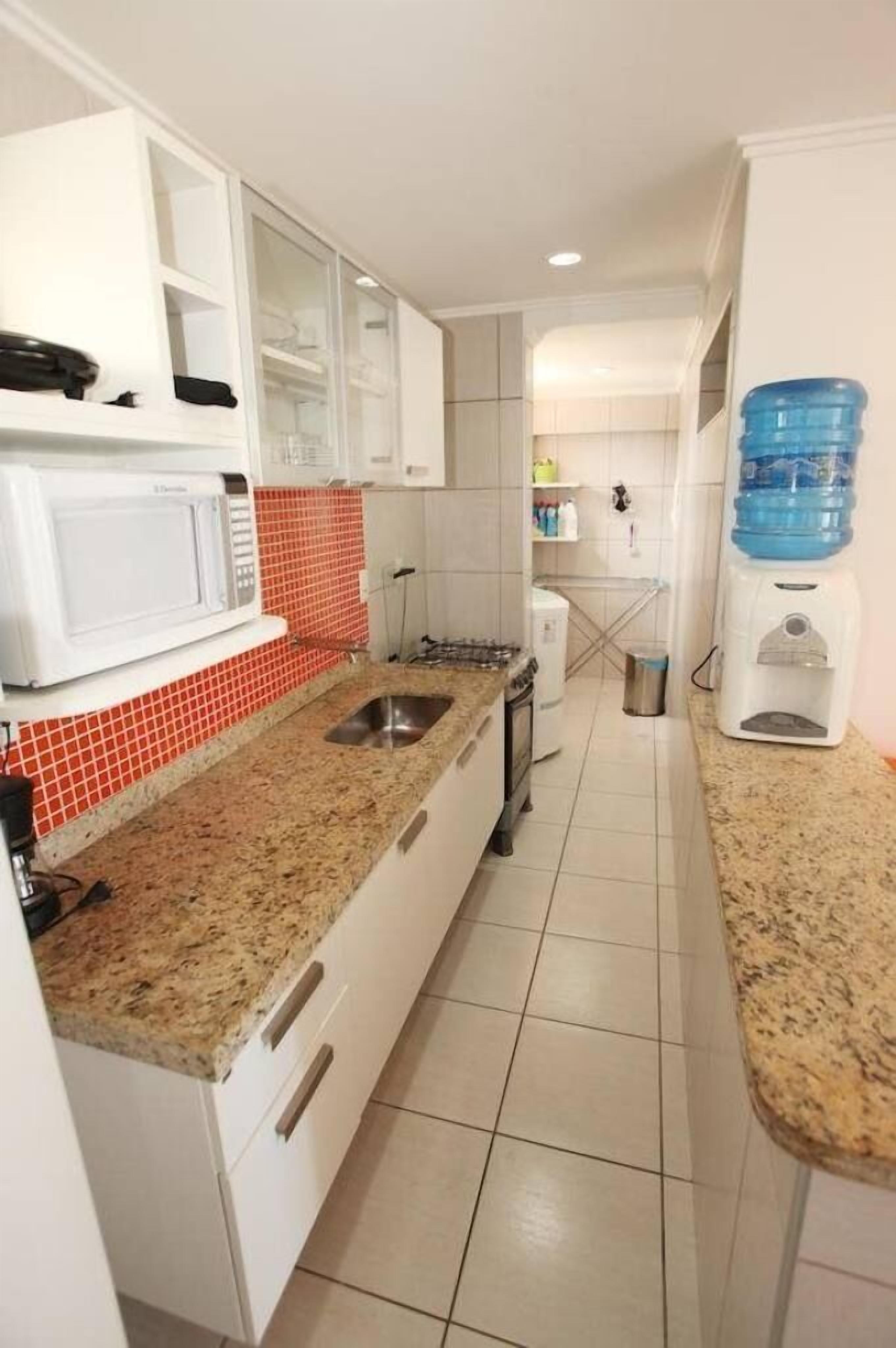 Una cocina con armarios blancos, encimera de granito, microondas, fregadero y dispensador de agua.
