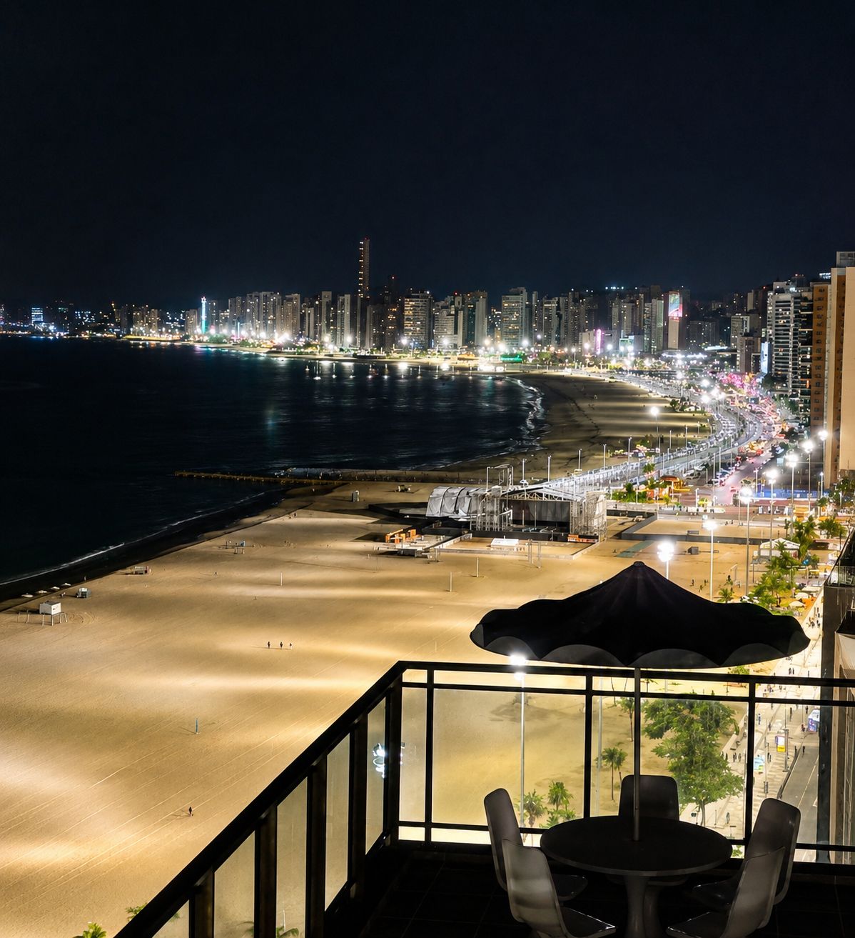 A balcony with a view of a beach and city skyline at night.
