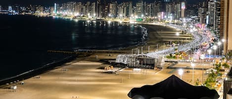 A balcony with a view of a beach and city skyline at night.