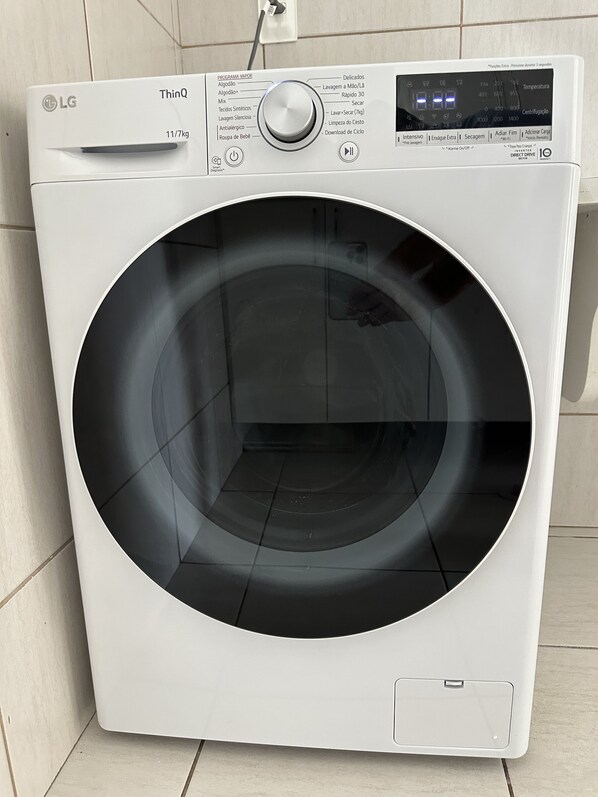 Un lave-linge à chargement frontal LG ThinQ blanc, doté d’un panneau de commande numérique, d’un câble d’alimentation et d’un petit tiroir de rangement.