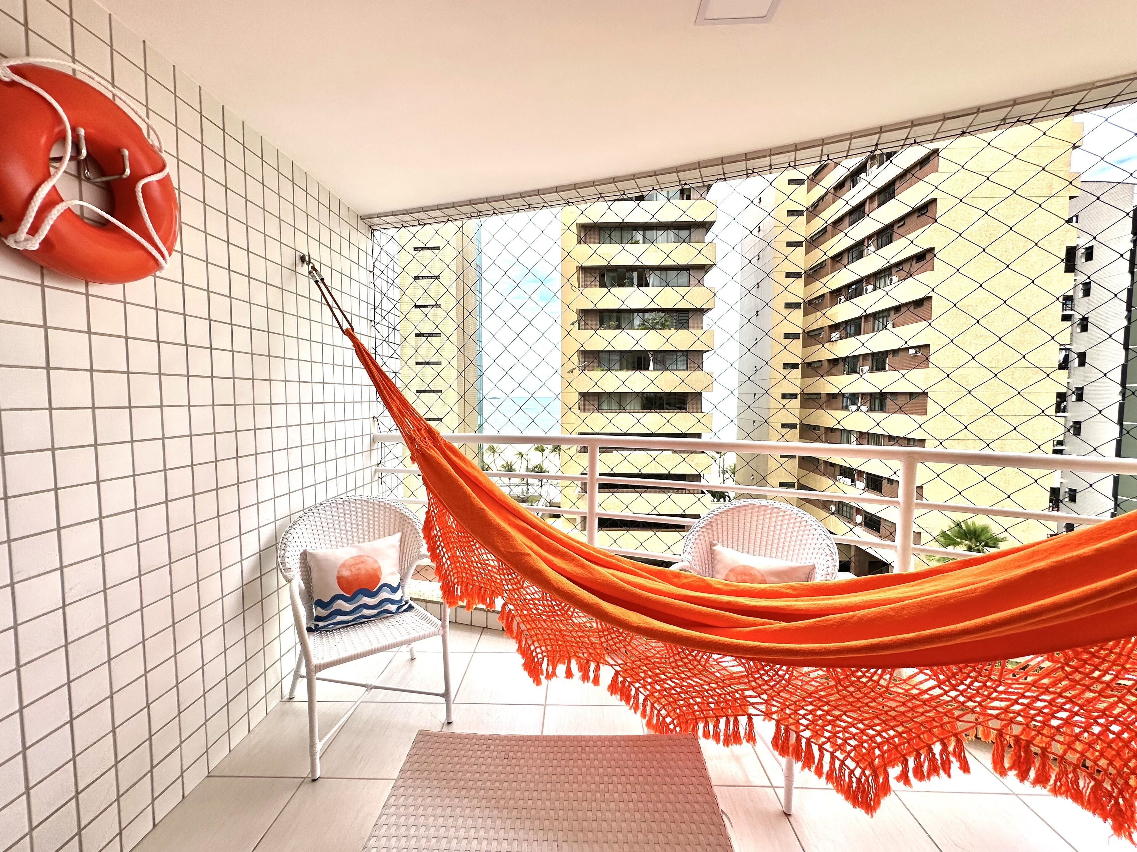 A balcony with a hammock, two chairs, and a life preserver on the wall.