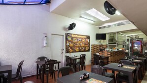 A restaurant with tables and chairs, a menu poster, a fire extinguisher, and a kitchen area.