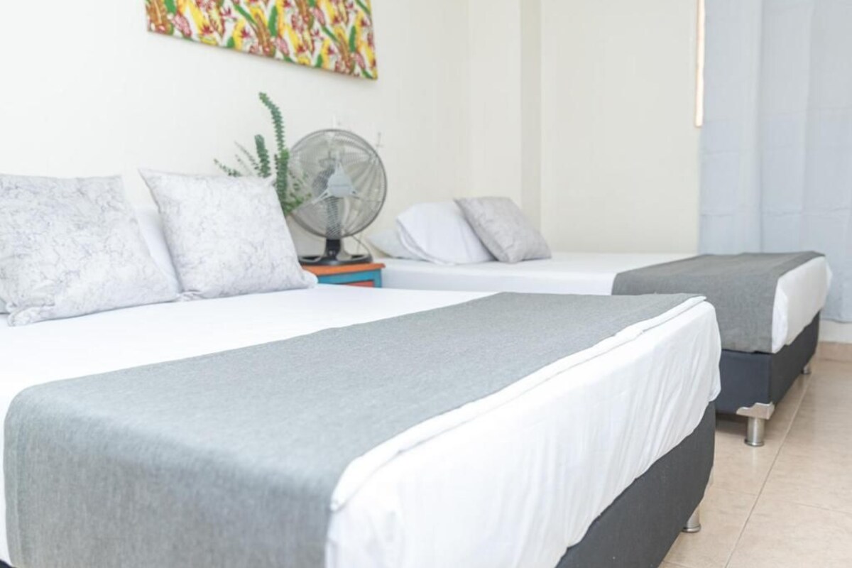 A hotel room with two beds, a fan, and a colorful painting on the wall.
