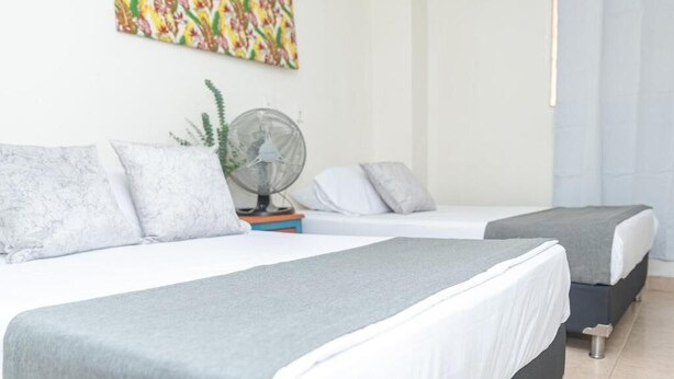 A hotel room with two beds, a fan, and a colorful painting on the wall.
