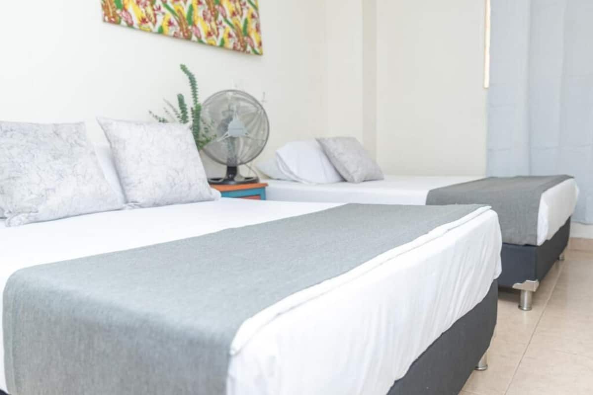 A hotel room with two beds, a fan, and a colorful painting on the wall.