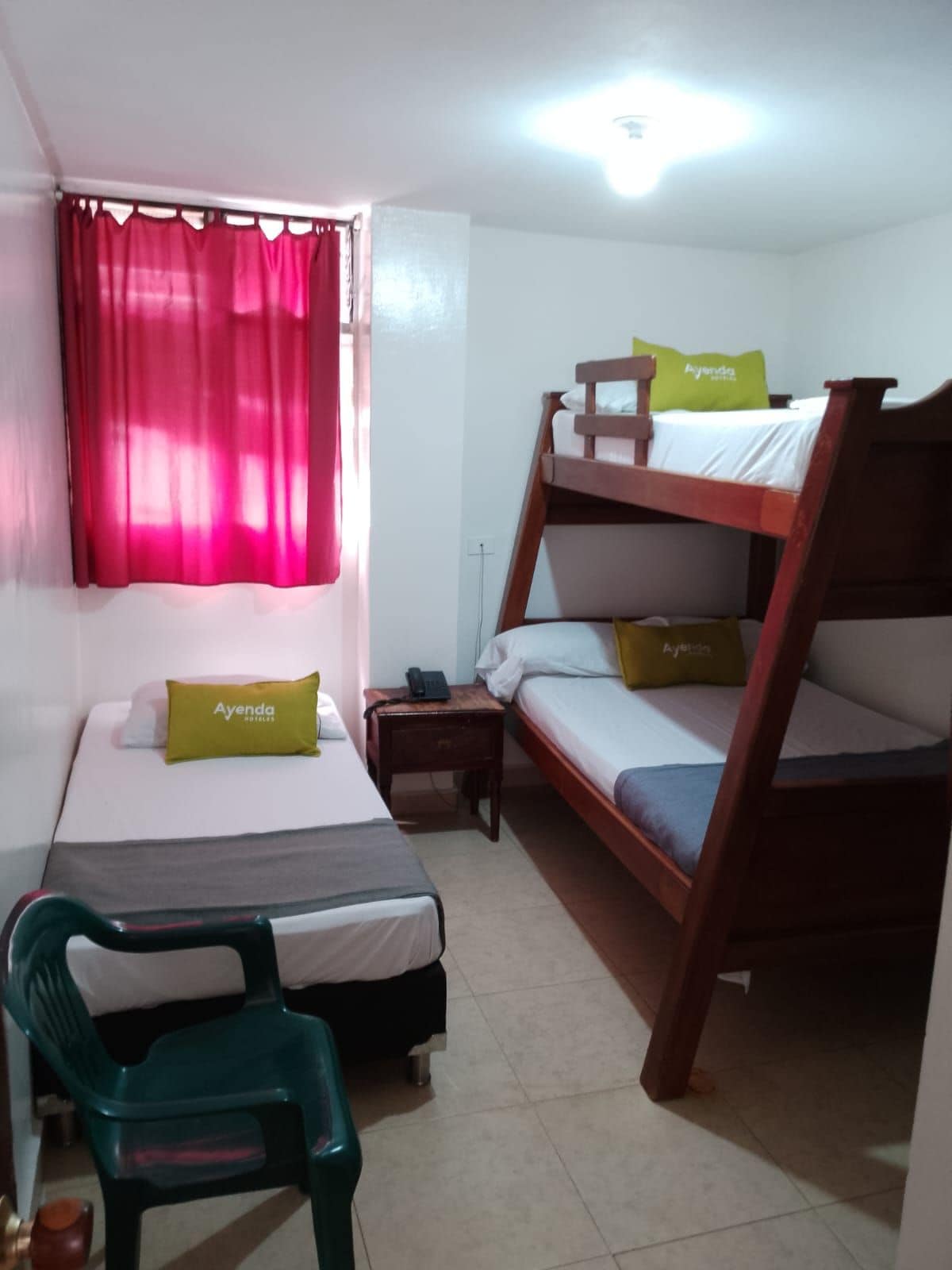 A dormitory room with bunk beds, a desk, a chair, and a window with curtains.