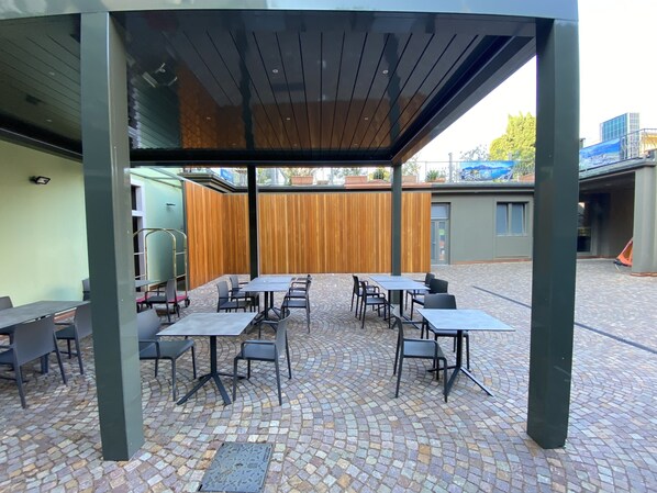 An outdoor patio with tables and chairs, a wooden fence, and a tiled floor.