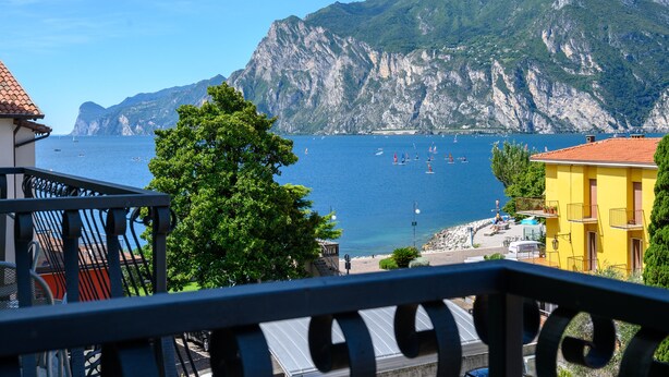 A coastal view with a mountain backdrop, a balcony with a railing, and a building with a red roof.