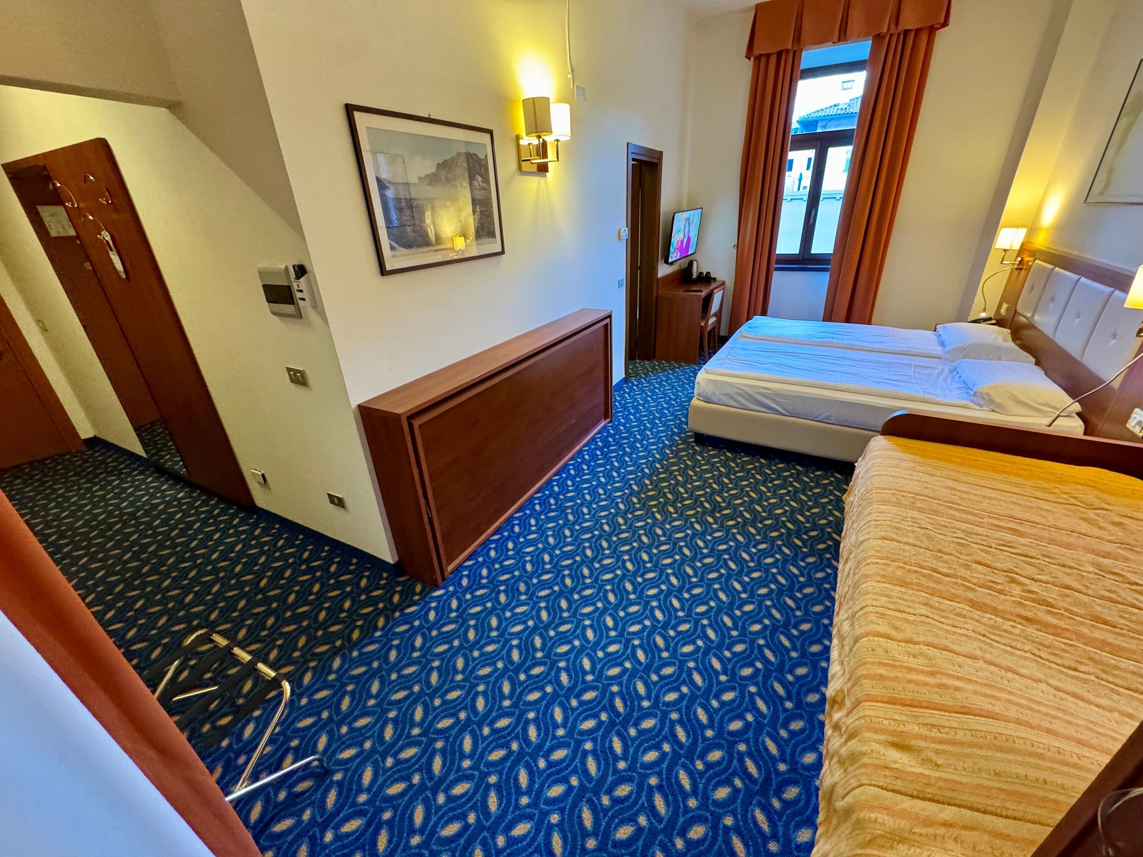Une chambre d’hôtel avec un grand lit, un bureau, une chaise, un téléviseur fixé au mur et une fenêtre avec des rideaux.