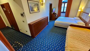 Une chambre d’hôtel avec un grand lit, un bureau, une chaise, un téléviseur fixé au mur et une fenêtre avec des rideaux.
