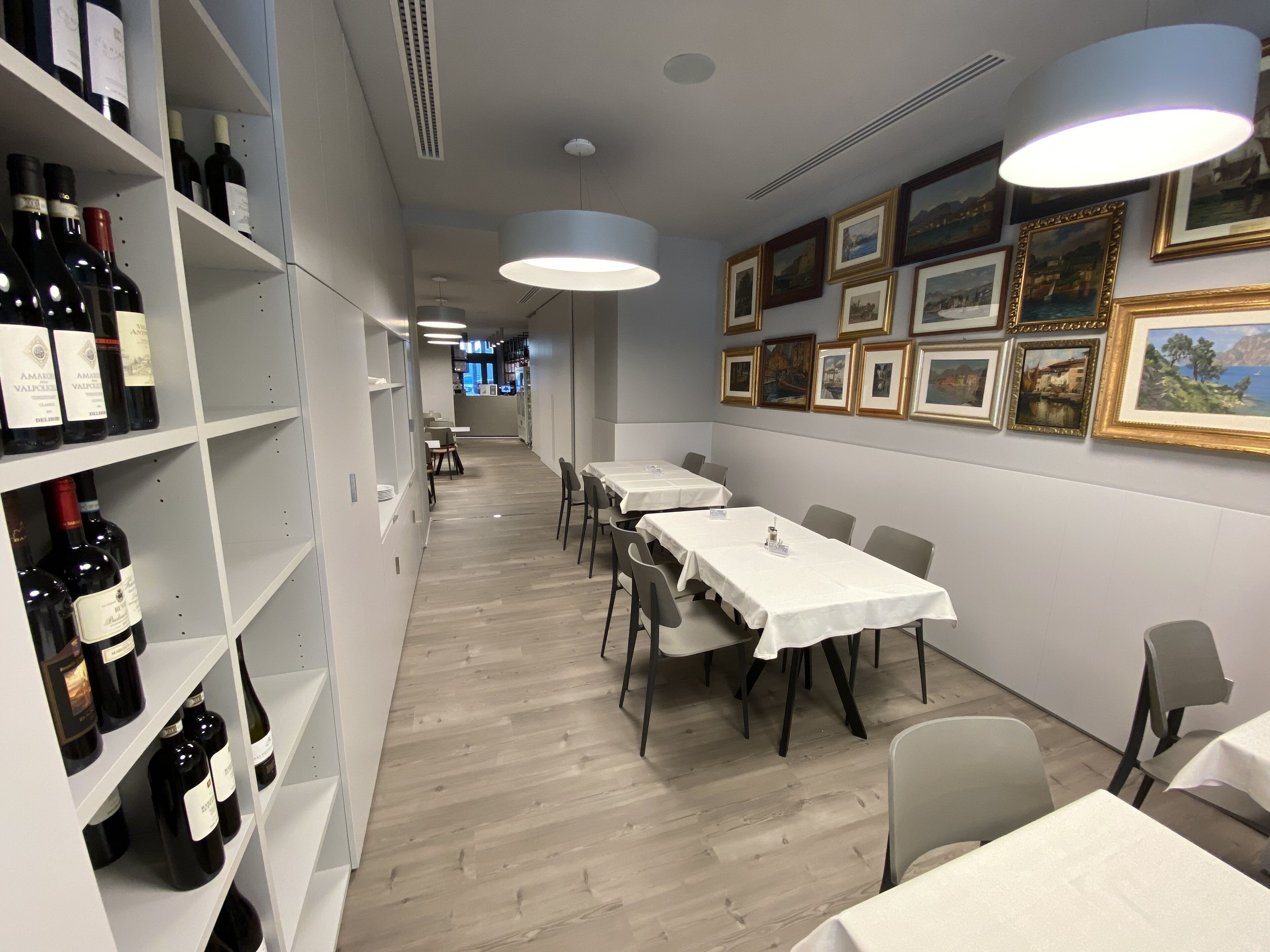 A restaurant with white tables and chairs, wine bottles on shelves, and framed pictures on the wall.