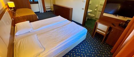 A hotel room with a double bed, a desk with a chair, a television, and a bathroom visible through an open door.