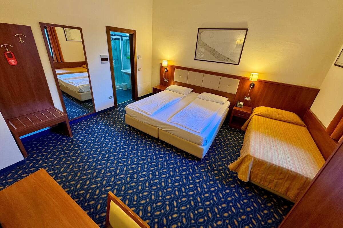 A hotel room with a large bed, a smaller bed, a desk, and a chair. There is a mirror on the wall and a framed picture above the smaller bed.