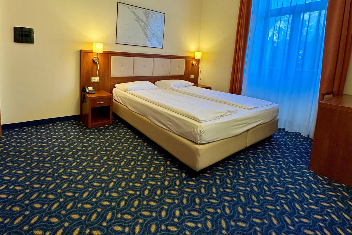 A hotel room with a large bed, two bedside tables with lamps, a map on the wall, and a patterned carpet.