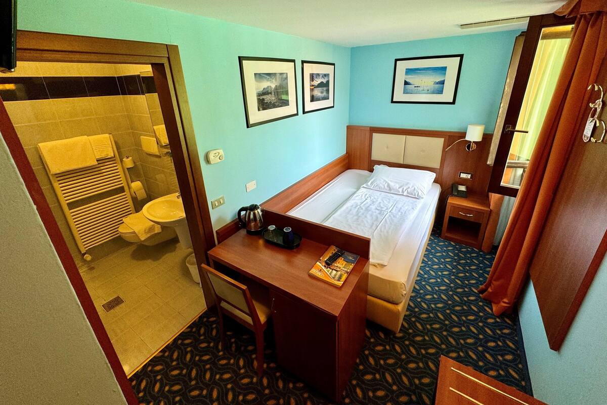 A hotel room with a bed, a desk, a chair, a bathroom, and a mirror.