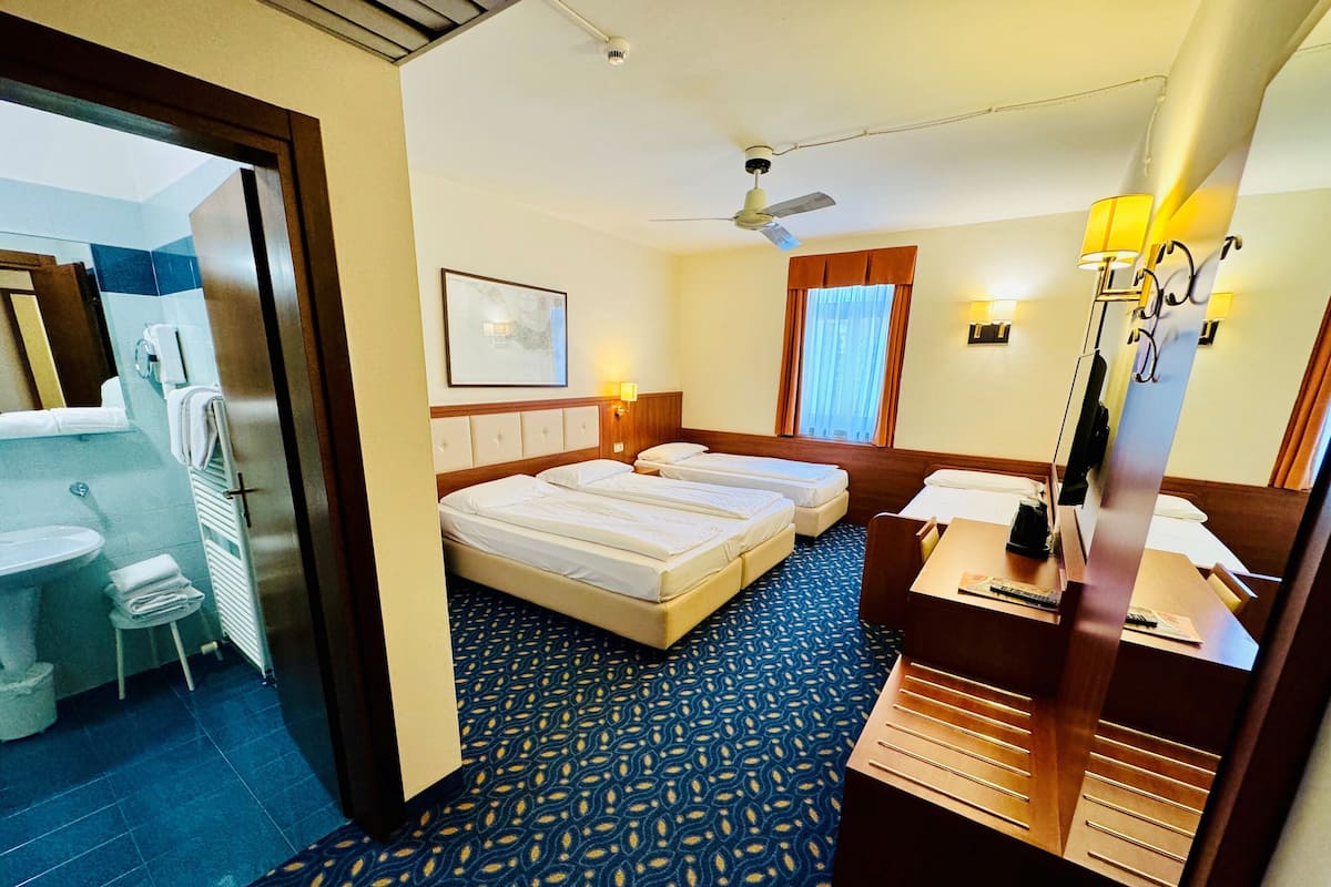 A hotel room with two beds, a desk, a chair, a bathroom, and a ceiling fan.