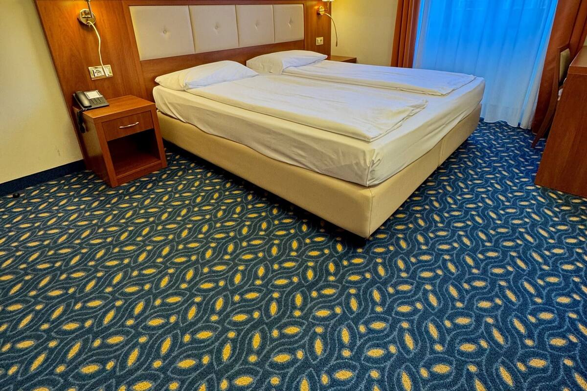 A hotel room with a large bed, two bedside tables with lamps, a telephone, and a window with curtains.