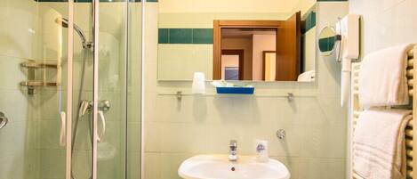 Un baño con ducha envuelta en vidrio, un lavamanos con espejo y un perchero para toallas.